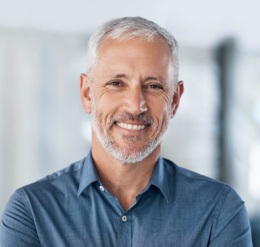 Smiling older man in a blue shirt representing confidence and expertise in biological dentistry at Biodental Health and Longevity.
