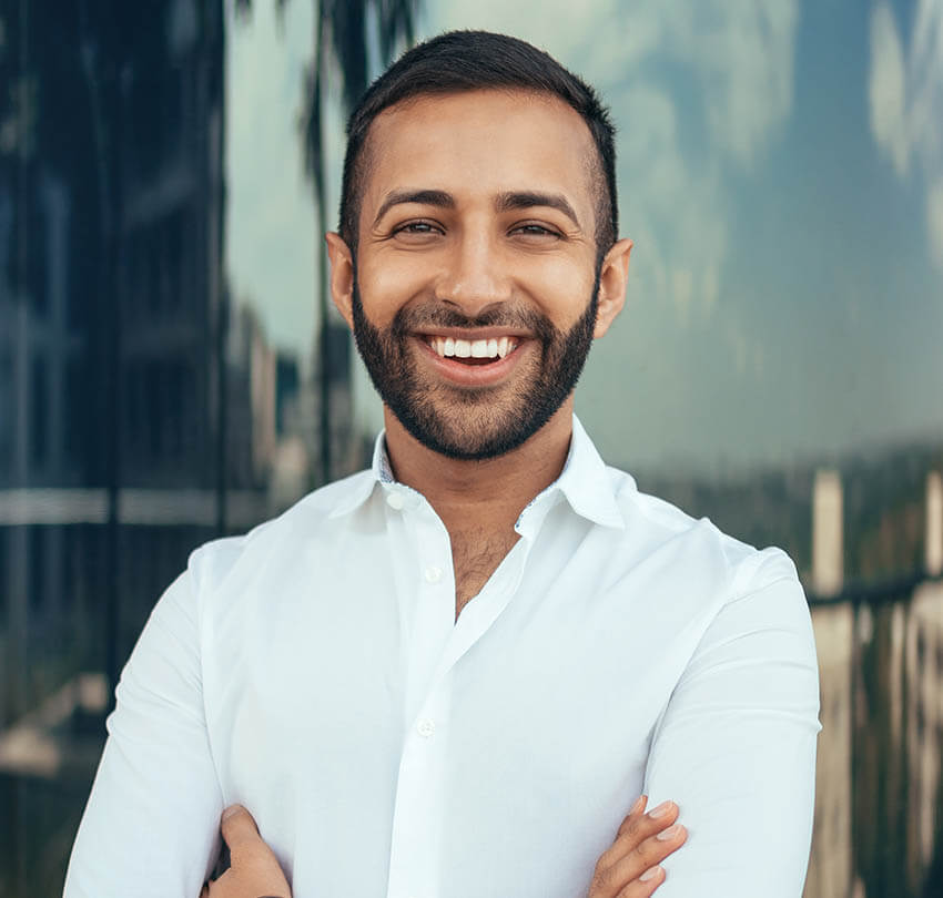 Smiling man in a white shirt, representing confidence and oral health, aligned with dental cleanings and exams at Biodental Health and Longevity in Pensacola.