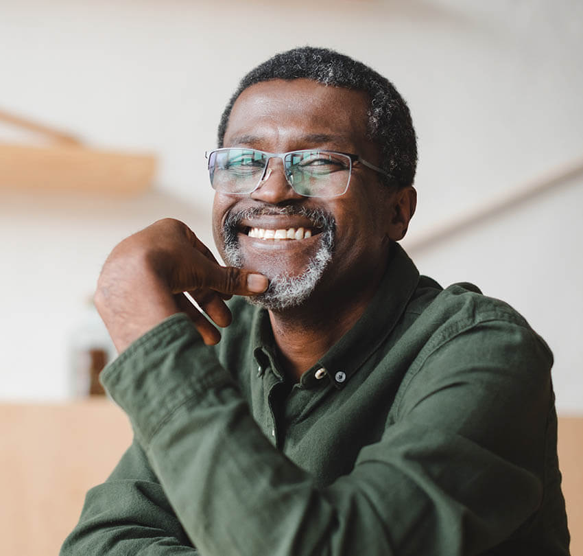 Smiling man with glasses in a green shirt, representing satisfaction and confidence after receiving dental crowns or bridges at Biodental Health and Longevity.