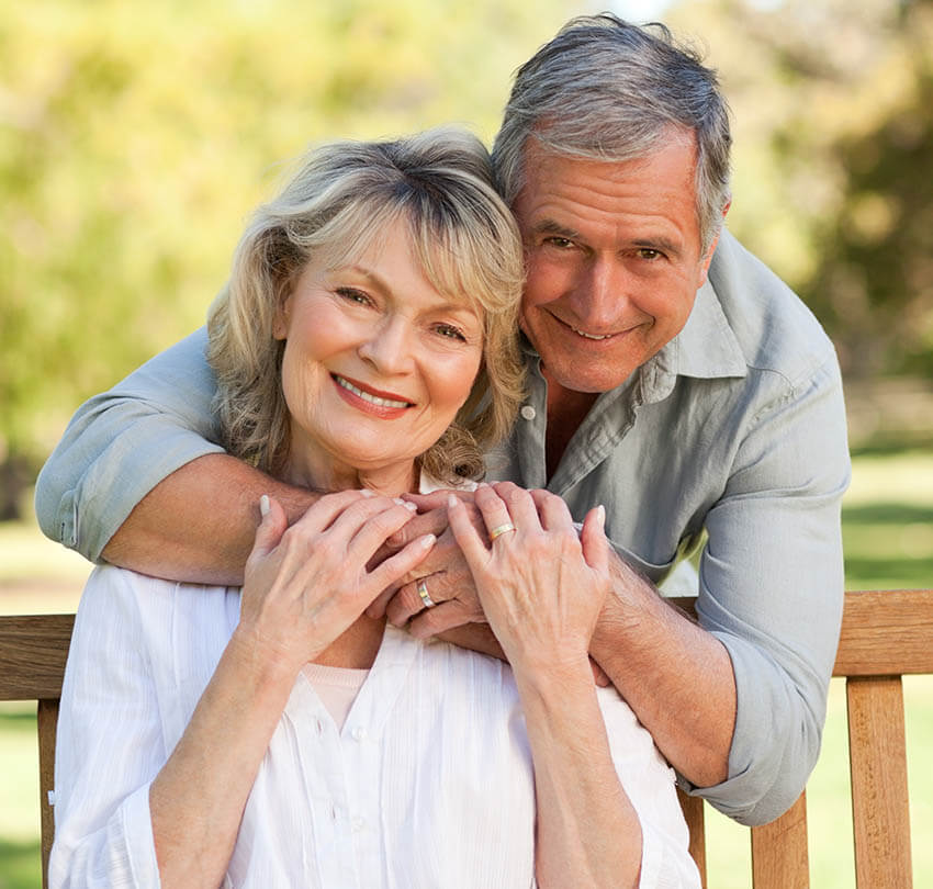 Smiling couple embracing outdoors, showcasing healthy smiles, representing the positive impact of dental implants on confidence and quality of life.