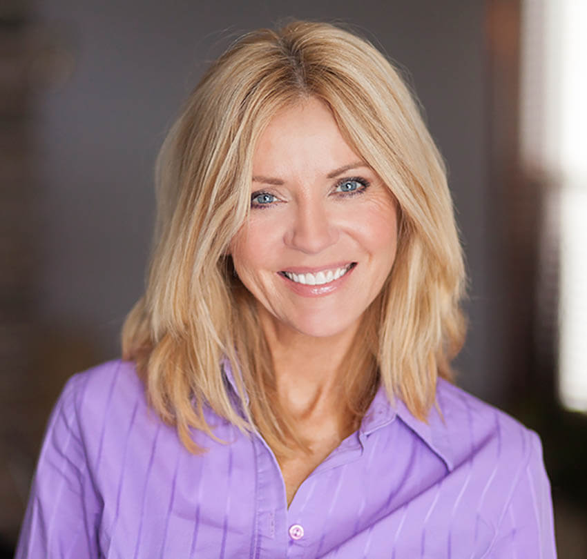 Smiling woman with blonde hair wearing a purple blouse, showcasing a bright and confident smile, representing the transformative effects of dental veneers.