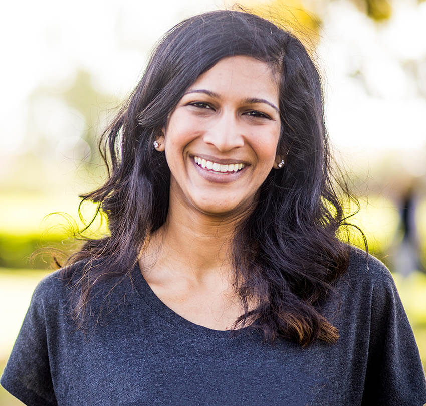 Smiling woman with long dark hair wearing a black shirt, representing the importance of maintaining a healthy smile in general dentistry.