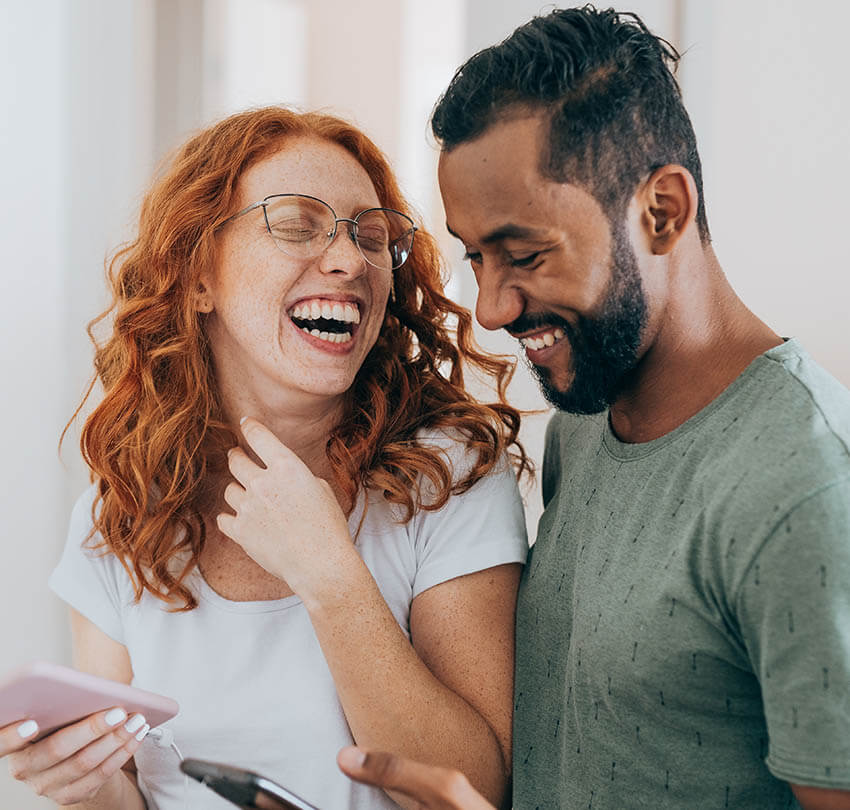 Laughing couple enjoying conversation while using smartphones, representing a friendly and engaging environment related to dental health discussions.