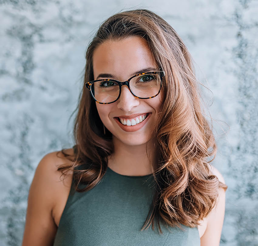 Smiling woman with glasses in a green top, representing wellness and health, in a modern setting related to holistic health treatments.
