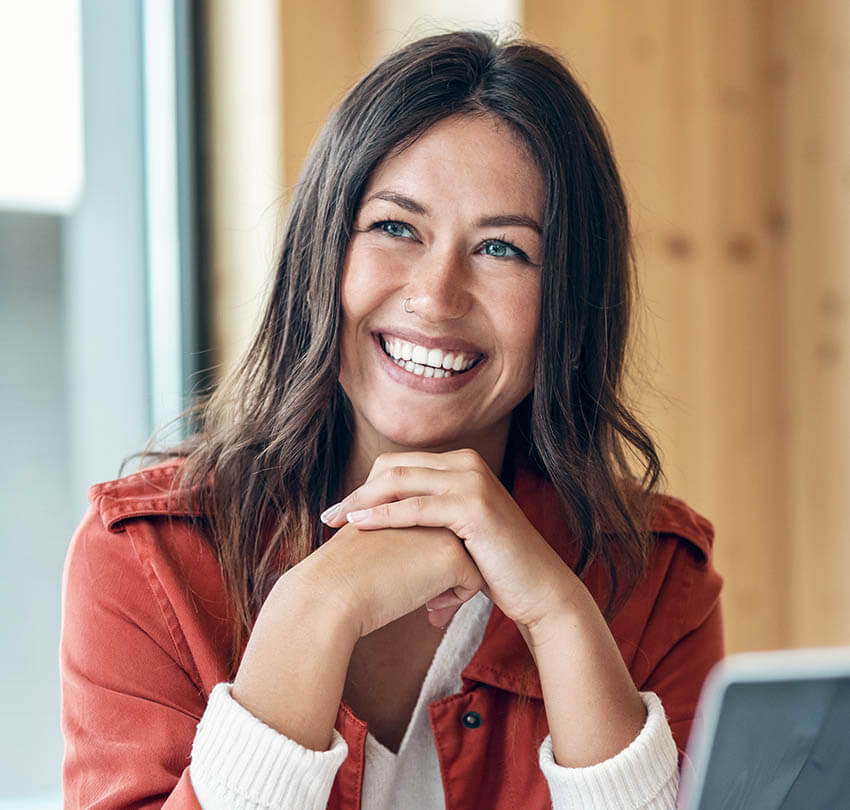 Smiling woman with long hair in an orange jacket, promoting wellness and confidence, representing red light therapy benefits at Biodental Health and Longevity in Pensacola.