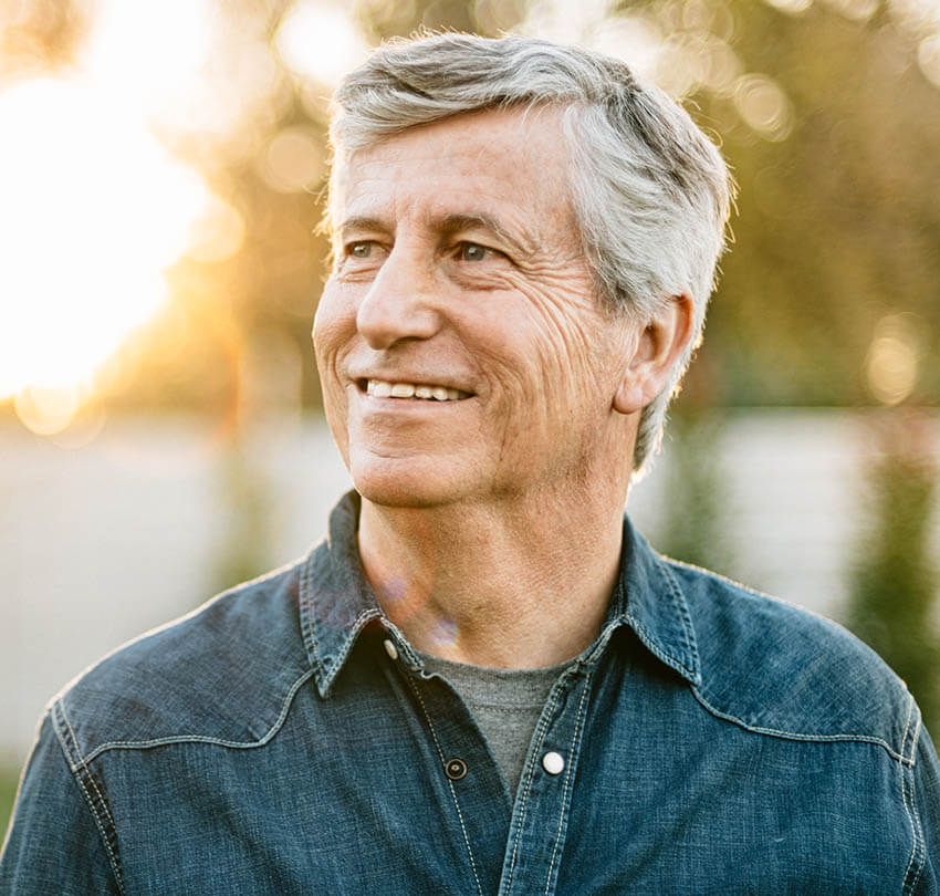 Smiling older man in a denim shirt, representing patient comfort and satisfaction in non-invasive dentistry at Biodental Health and Longevity.