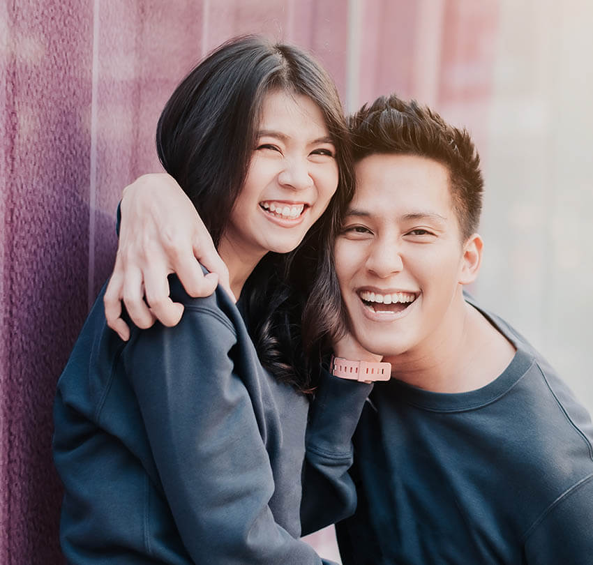 Happy couple smiling together against a purple background, showcasing joy and connection, relevant to promoting a comfortable and holistic approach to oral surgery services.