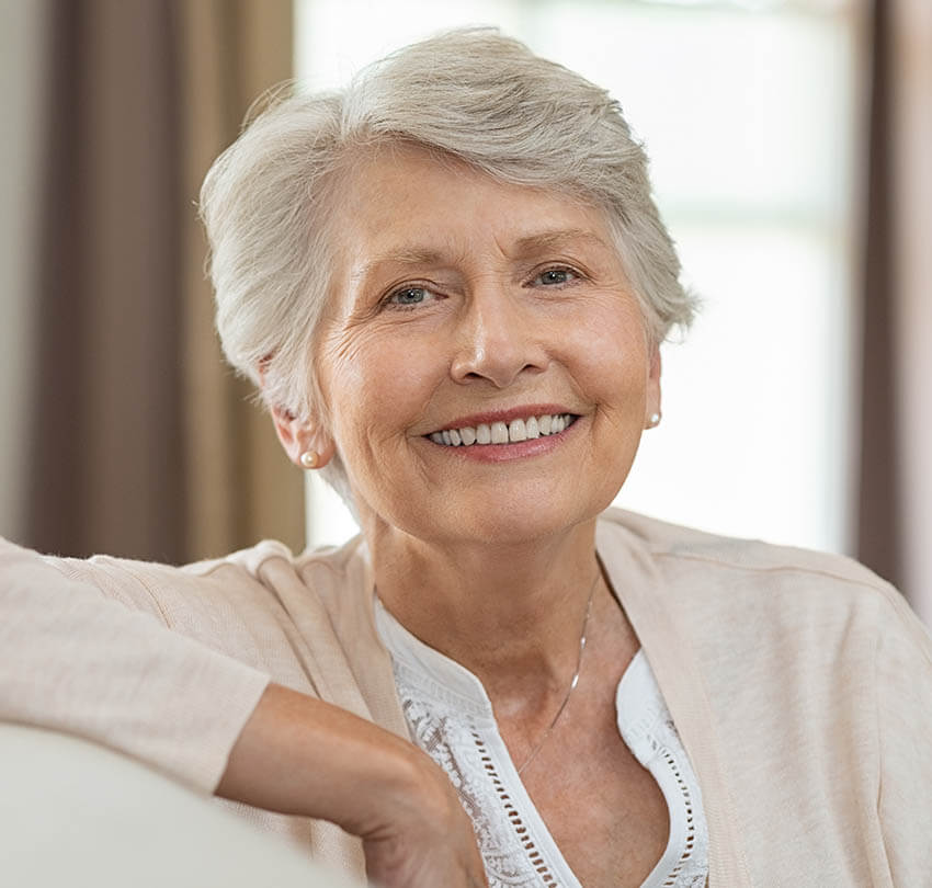 Smiling older woman with short gray hair in a cozy indoor setting, representing wellness and vitality related to personalized health services.