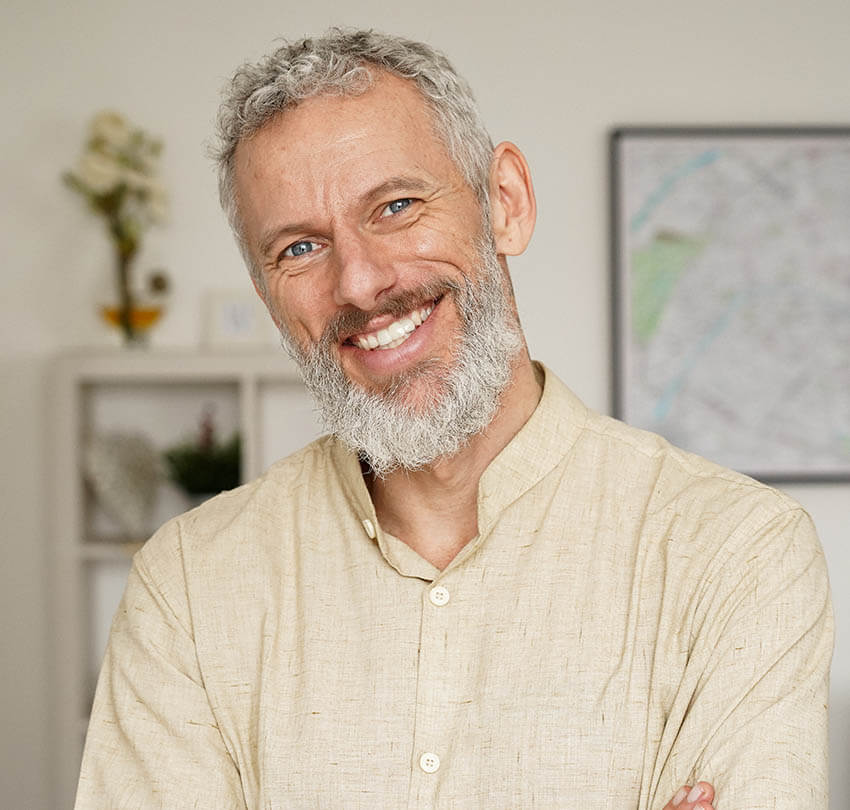 Smiling man with a beard in a light-colored shirt, showcasing a confident and friendly demeanor, representing the positive impact of cosmetic dentistry and tooth bonding.