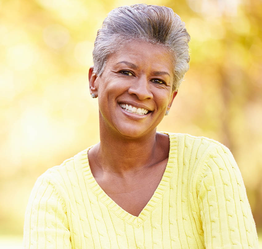 Smiling woman in a yellow sweater, representing comfort and well-being, emphasizing holistic dental care at Biodental Health and Longevity in Pensacola.