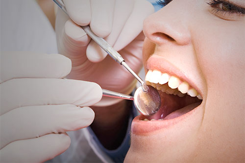 Dental professional examining a patient's mouth with a dental mirror and explorer, highlighting the importance of dental cleanings for oral health.