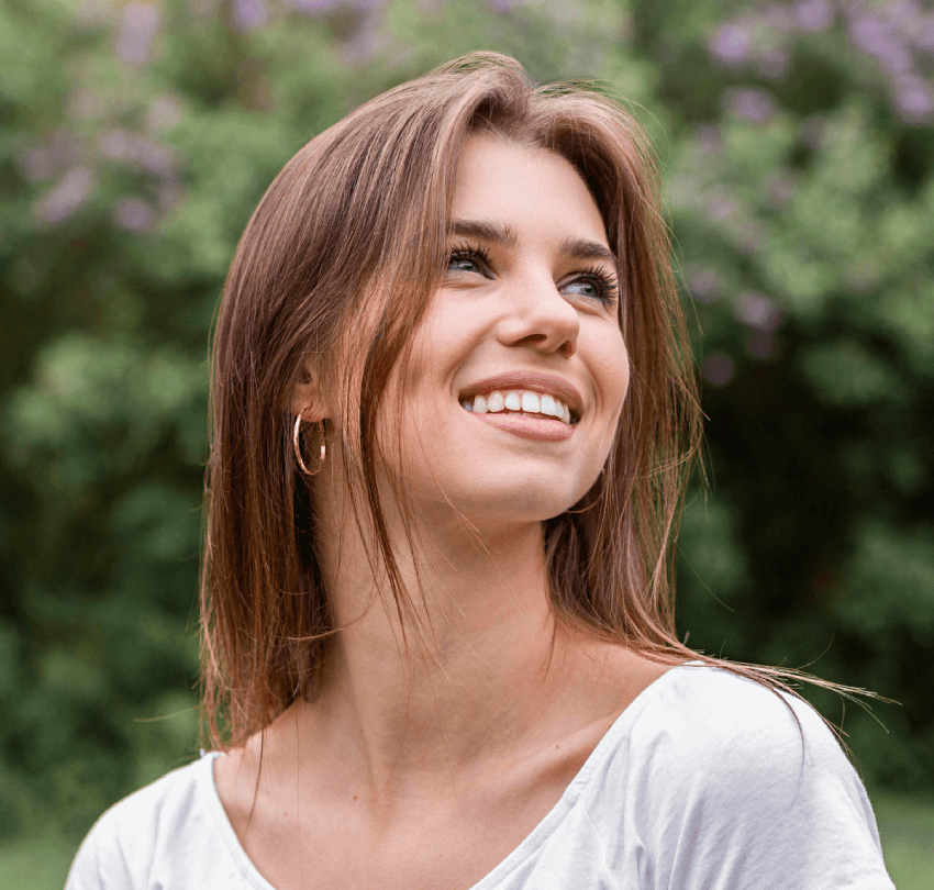 Young woman smiling confidently outdoors, showcasing a bright, healthy smile, emphasizing the benefits of cosmetic dentistry and smile makeovers.