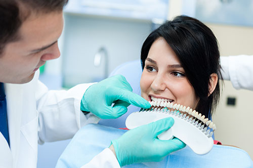 Dentist showing dental veneers shade guide to a patient, highlighting cosmetic dentistry options for a healthier, more confident smile.