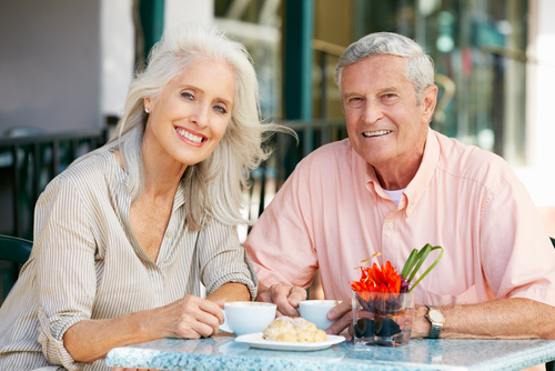 Smiling older couple enjoying coffee and pastries at a table, representing confidence and joy in social interactions, relevant to discussions on dental implants and restoring smiles.