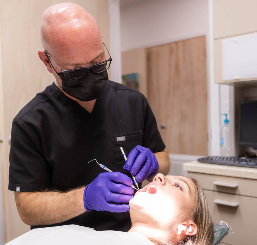 Dentist performing a dental cleaning on a patient in a clinical setting, highlighting the importance of oral health and preventive care at Biodental Health and Longevity in Pensacola.