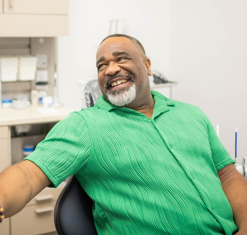 Smiling man in green shirt sitting in dental chair, showcasing positive experience at restorative dentistry appointment in Pensacola.