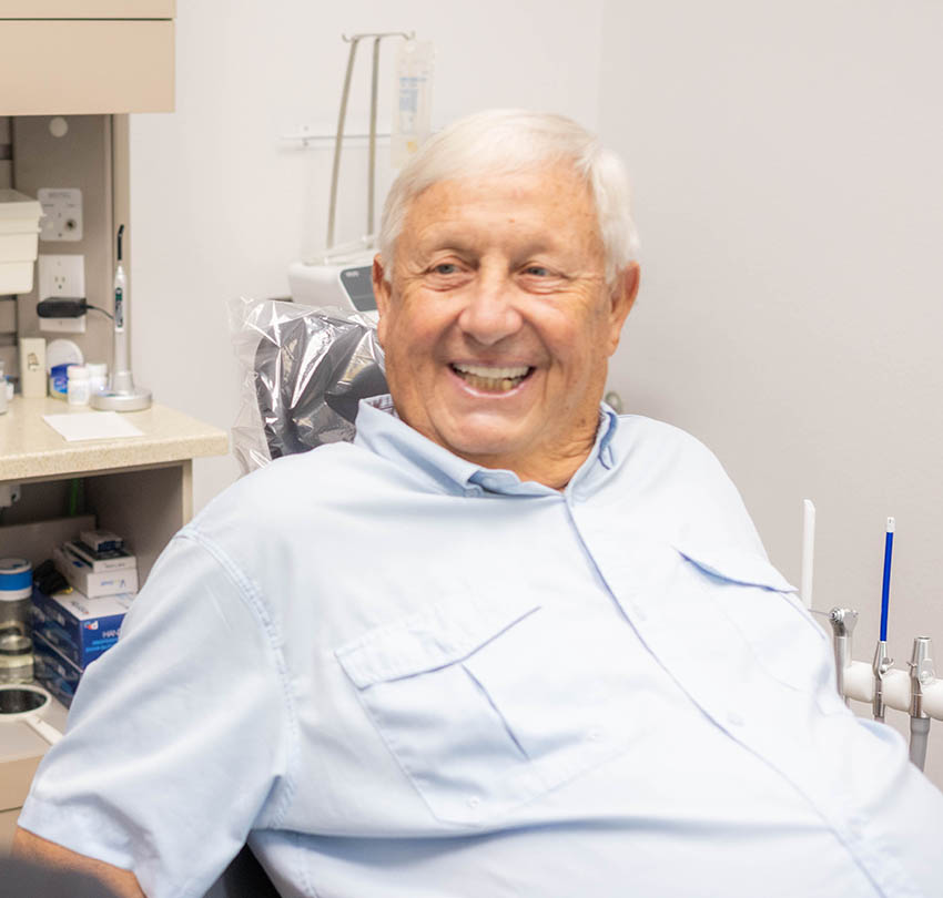 Smiling elderly man in dental chair at Biodental Health and Longevity, showcasing patient satisfaction with All-on-X dental implants.