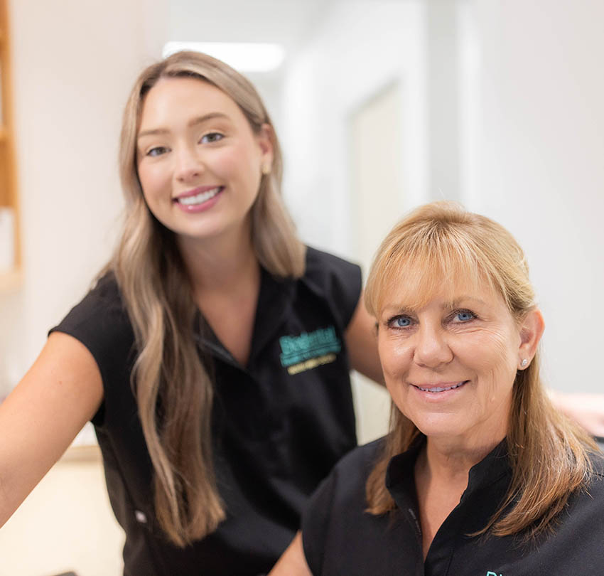 Two smiling staff members at Biodental Health and Longevity in Pensacola, wearing black uniforms, promoting a welcoming atmosphere for whole-body health and advanced dental care.