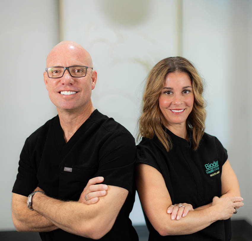 Dentists at Biodental Health and Longevity, smiling confidently in black scrubs, promoting dental care and services.