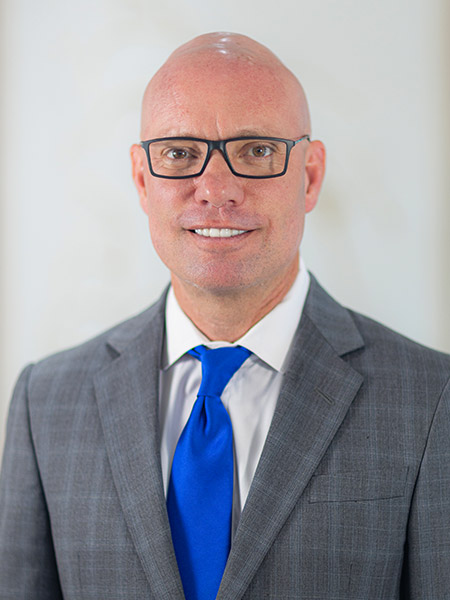 Dr. Christopher M. Campus, dentist in Pensacola, wearing a gray suit and blue tie, smiling against a light background.